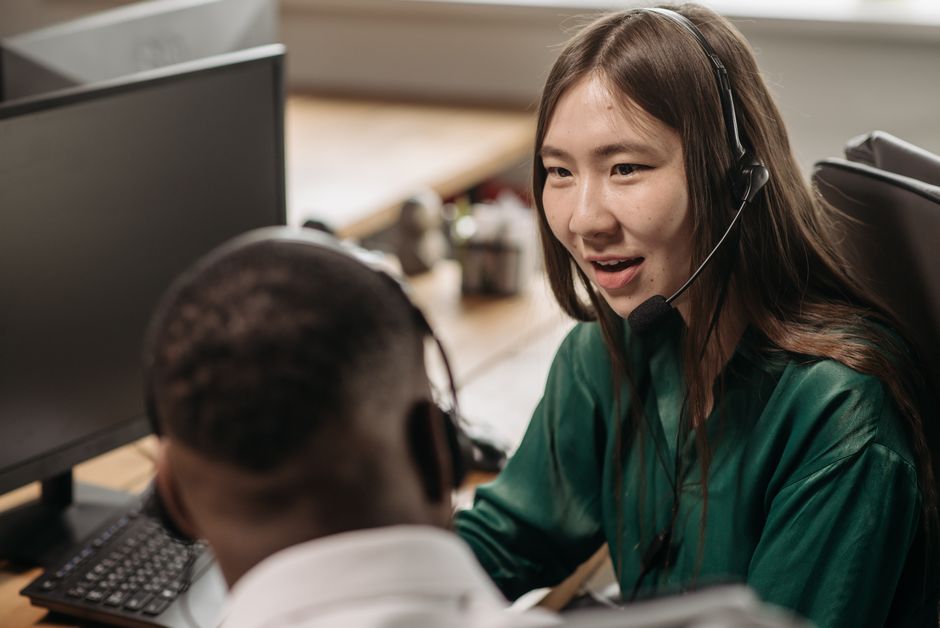 Jovem mulher asiática em um call center conversando com um colega em um ambiente de escritório.