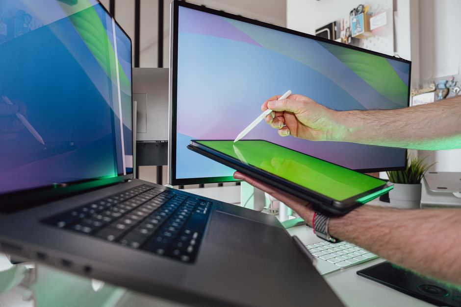 Uma pessoa usando uma caneta stylus em um tablet em um espaço de trabalho tecnológico com monitores duplos