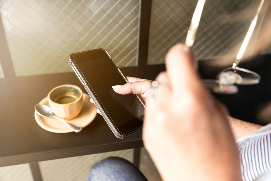 Pessoa verificando smartphone ao lado de café na mesa, dentro de casa.